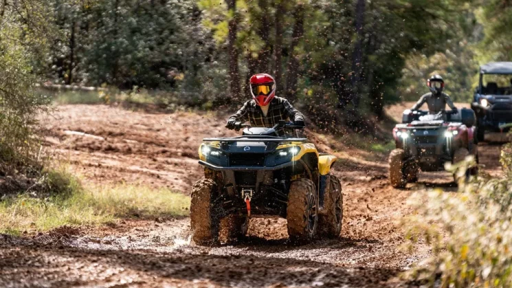 Three Outlander 500/700 ATVs follow one another on a muddy trail.